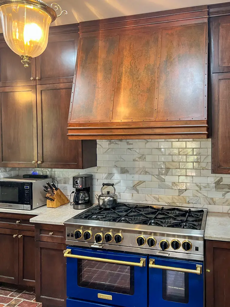 Custom copper range hood with wood trim above blue Viking stove