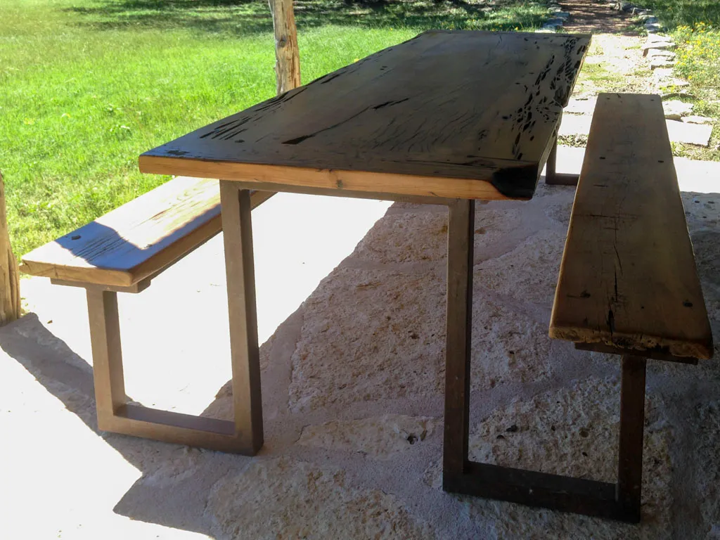 Outdoor dining table and bench set with metal legs on stone patio